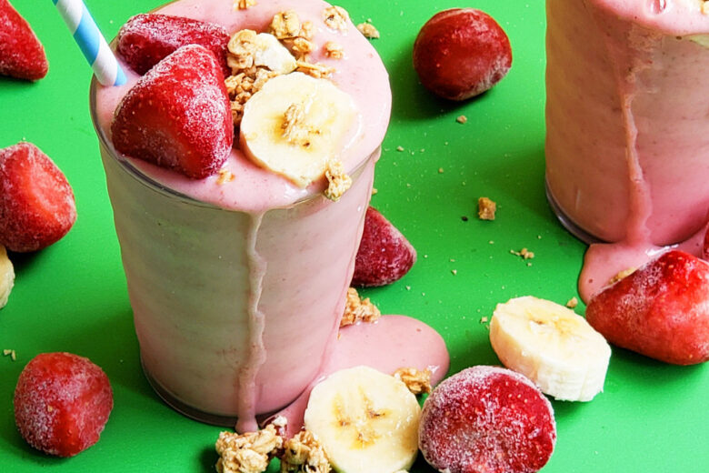 banana strawberry oat smoothie in a clear glass topped with frozen strawberries, bananas, and granola