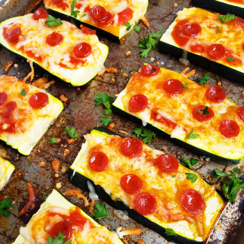 Mini Zucchini Pizza Boats, sliced zucchini topped with mozzarella cheese and mini pepperoni on a cookie sheet