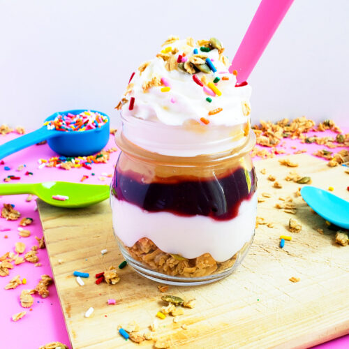 PB&J Greek Yogurt Parfait made with Bob's Red Mill Granola, peanut butter and jelly and sprinkles on a pink surface