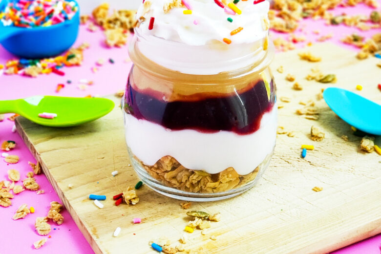 PB&J Greek Yogurt Parfait made with Bob's Red Mill Granola, peanut butter and jelly and sprinkles on a pink surface