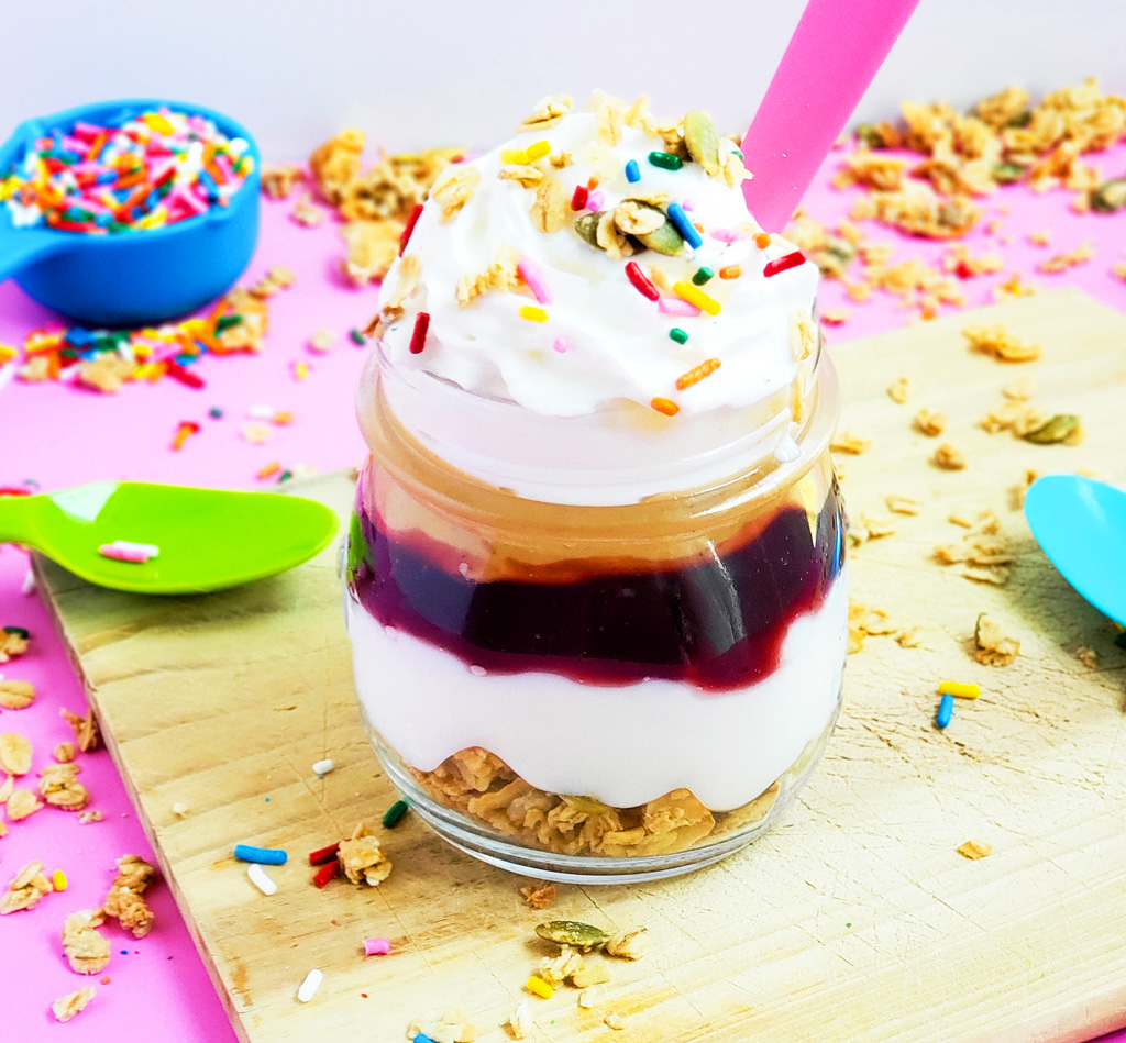 PB&J Greek Yogurt Parfait made with Bob's Red Mill Granola, peanut butter and jelly and sprinkles on a pink surface