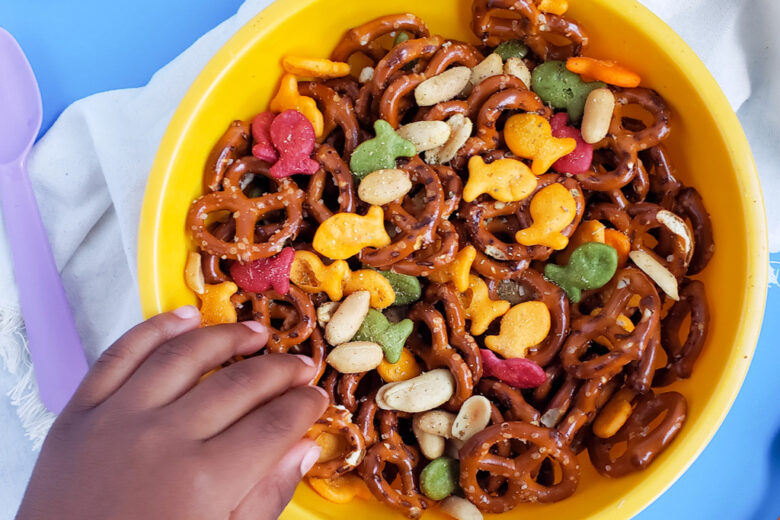 CJs Rockstar Trail Mix made with multi-colored goldfish crackers, pretzels, and peanuts in a yellow bowl on a blue surface