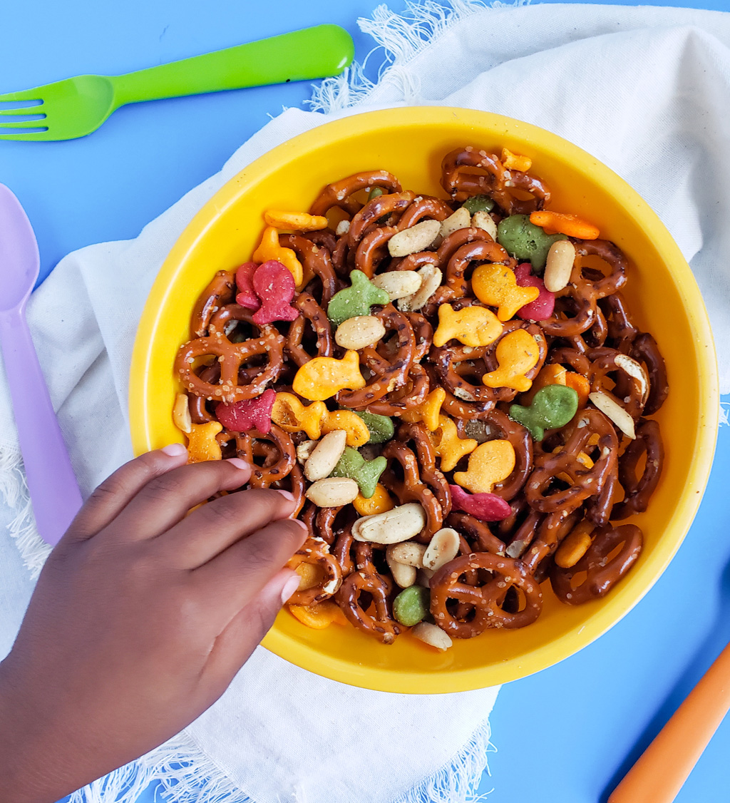 CJs Rockstar Trail Mix made with multi-colored goldfish crackers, pretzels, and peanuts in a yellow bowl on a blue surface