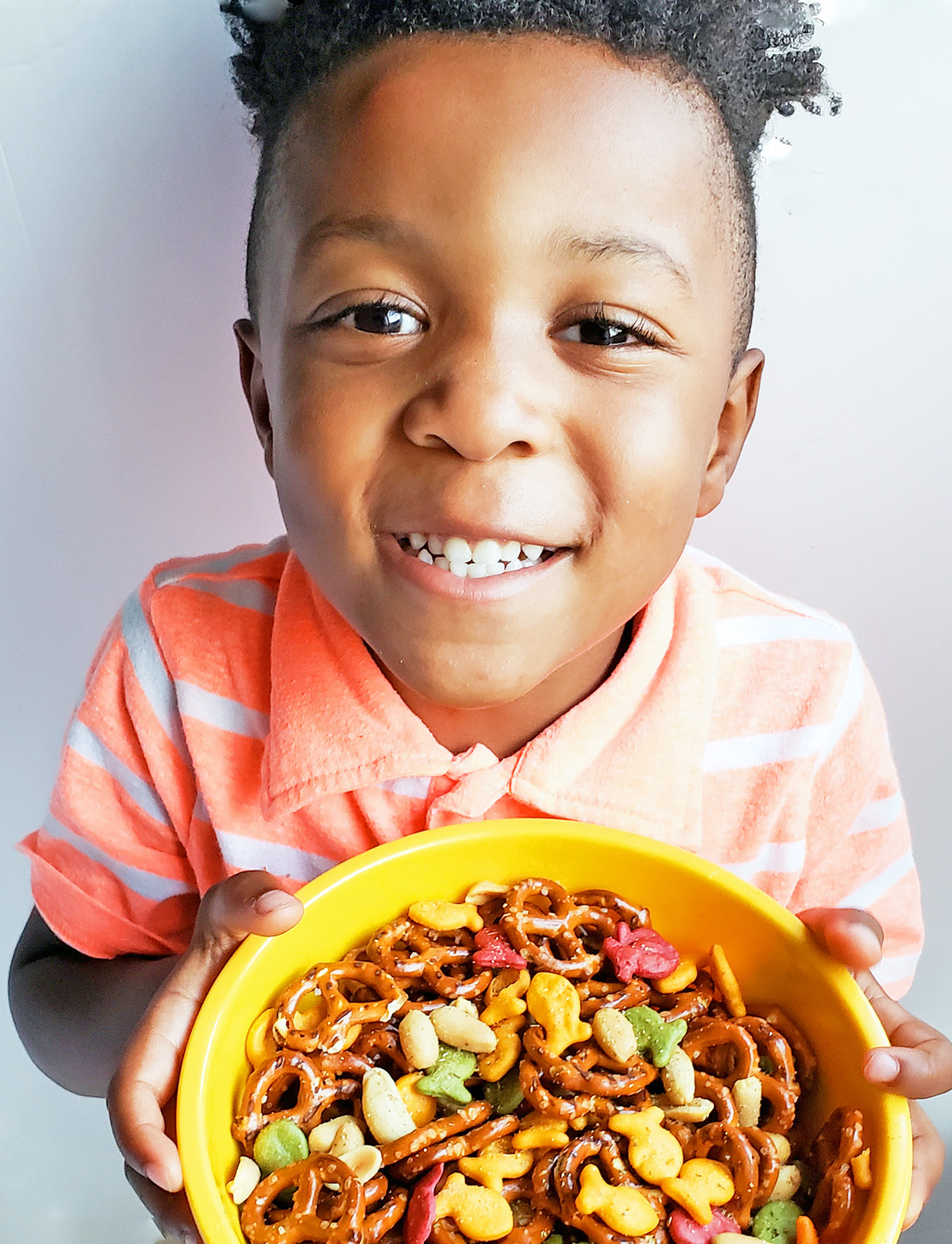 CJs Rockstar Trail Mix made with multi-colored goldfish crackers, pretzels, and peanuts in a yellow bowl on a blue surface