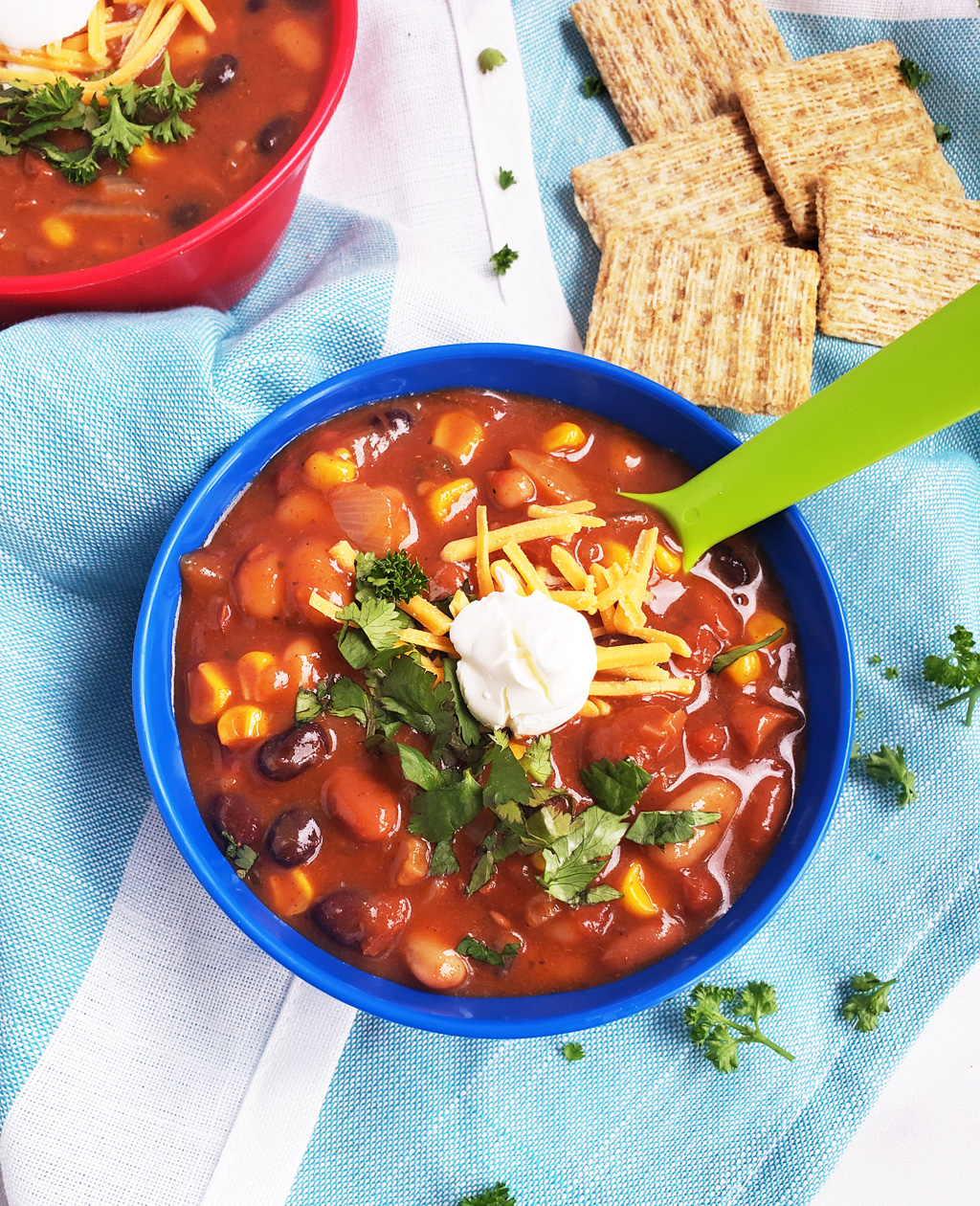 Simple Vegetarian Taco Soup, the perfect meatless meal, topped with green onion, cheese, and sour cream, served in a kid-friendly blue bowl with a green spoon. #tacosoup #vegetarianmeals #plantbasedkids #plantbasedmeals #plantbasedkidmeals