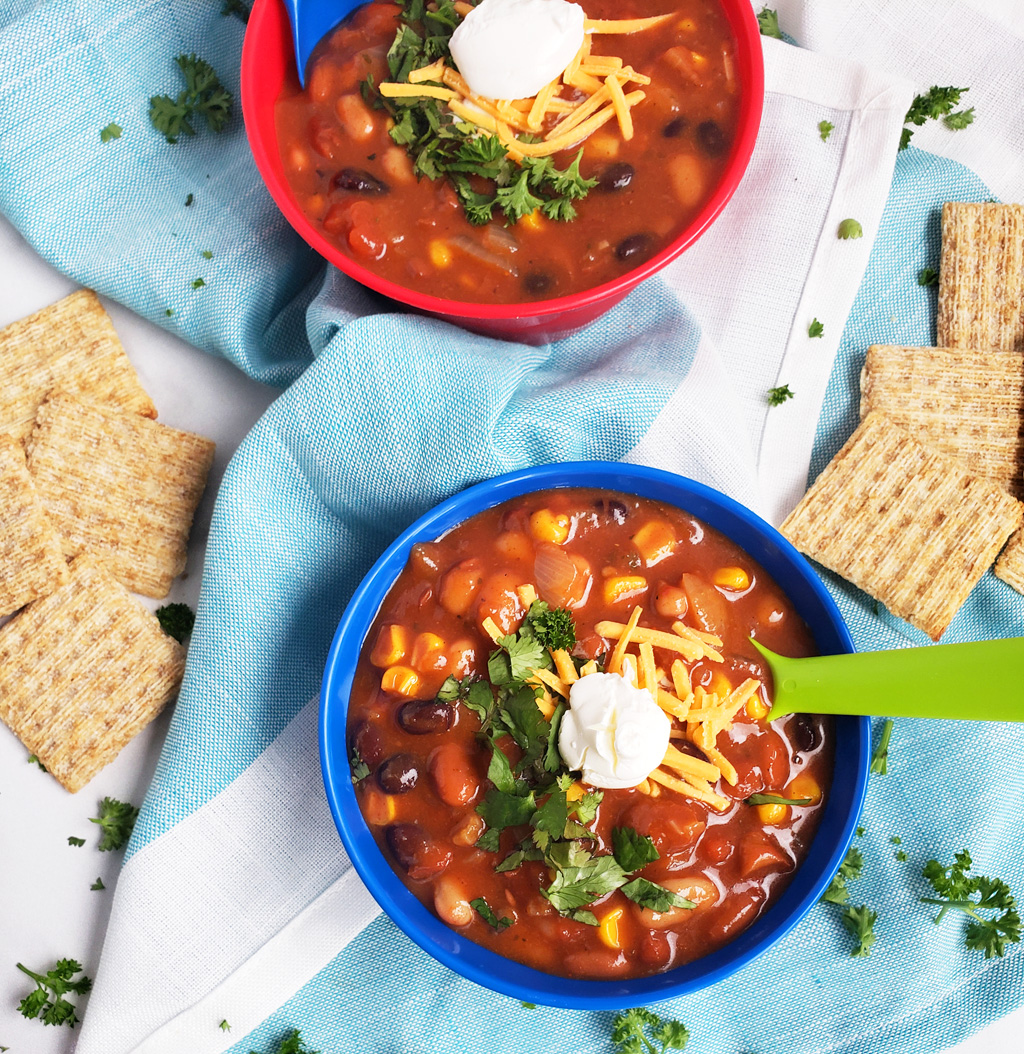 Simple Vegetarian Taco Soup, the perfect meatless meal, topped with green onion, cheese, and sour cream, served in a kid-friendly blue bowl with a green spoon. #tacosoup #vegetarianmeals #plantbasedkids #plantbasedmeals #plantbasedkidmeals