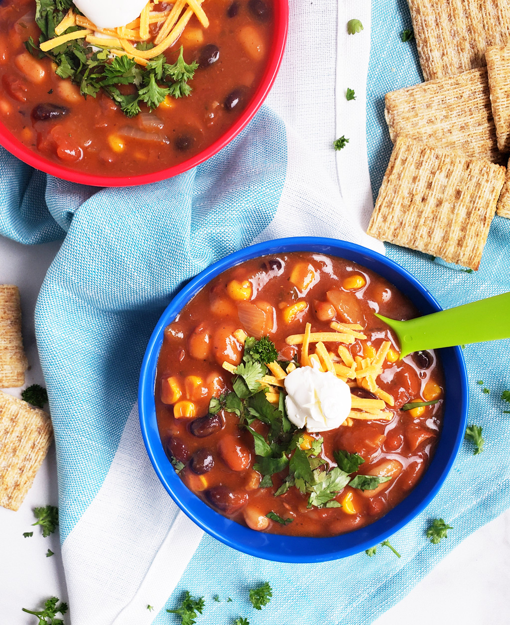 Simple Vegetarian Taco Soup, the perfect meatless meal, topped with green onion, cheese, and sour cream, served in a kid-friendly blue bowl with a green spoon. #tacosoup #vegetarianmeals #plantbasedkids #plantbasedmeals #plantbasedkidmeals