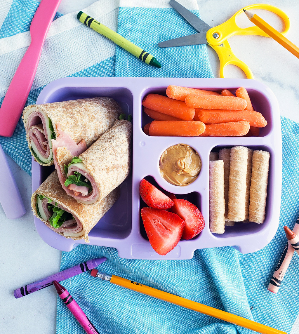 Bento box filled and arranged beautifully with fruits, veggies, whole wheat ham and cheese wraps. Healthy bento lunch ideas for kids. Littleeatsandthings.com 