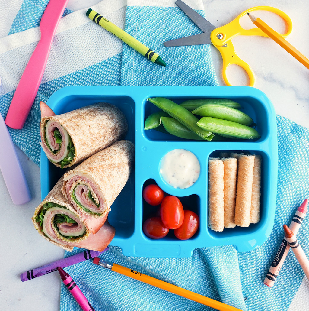 Bento box filled and arranged beautifully with fruits, veggies, whole wheat ham and cheese wraps. Healthy bento lunch ideas for kids. Littleeatsandthings.com 