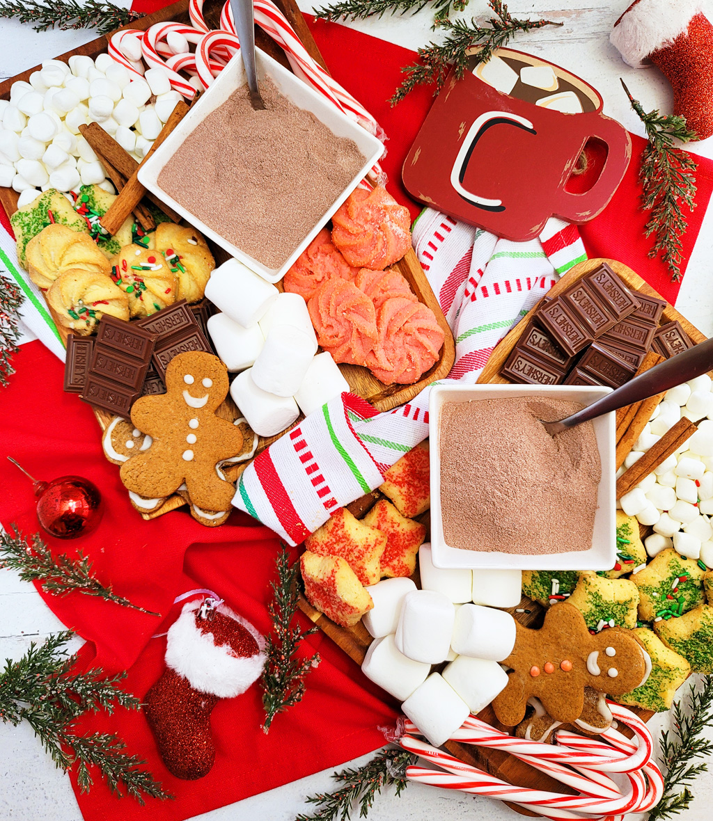 DIY Holiday Hot Cocoa Charcuterie Board on a wooden cutting board with gingerbread cookies, marshmallows, and hot chocolate mix. The perfect Christmas charcuterie board. www.littleeatsandthings.com 