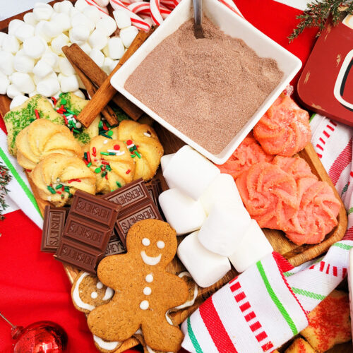 DIY Holiday Hot Cocoa Charcuterie Board on a wooden cutting board with gingerbread cookies, marshmallows, and hot chocolate mix. The perfect Christmas charcuterie board. www.littleeatsandthings.com