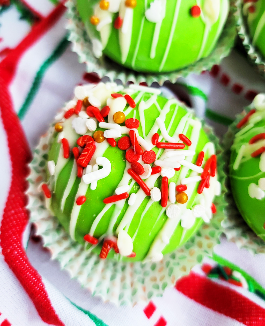 Green Grinch hot chocolate bombs with white chocolate drizzled on top, with Christmas sprinkles. DIY Hot chocolate bomb recipe. www.littleeatsandthings.com