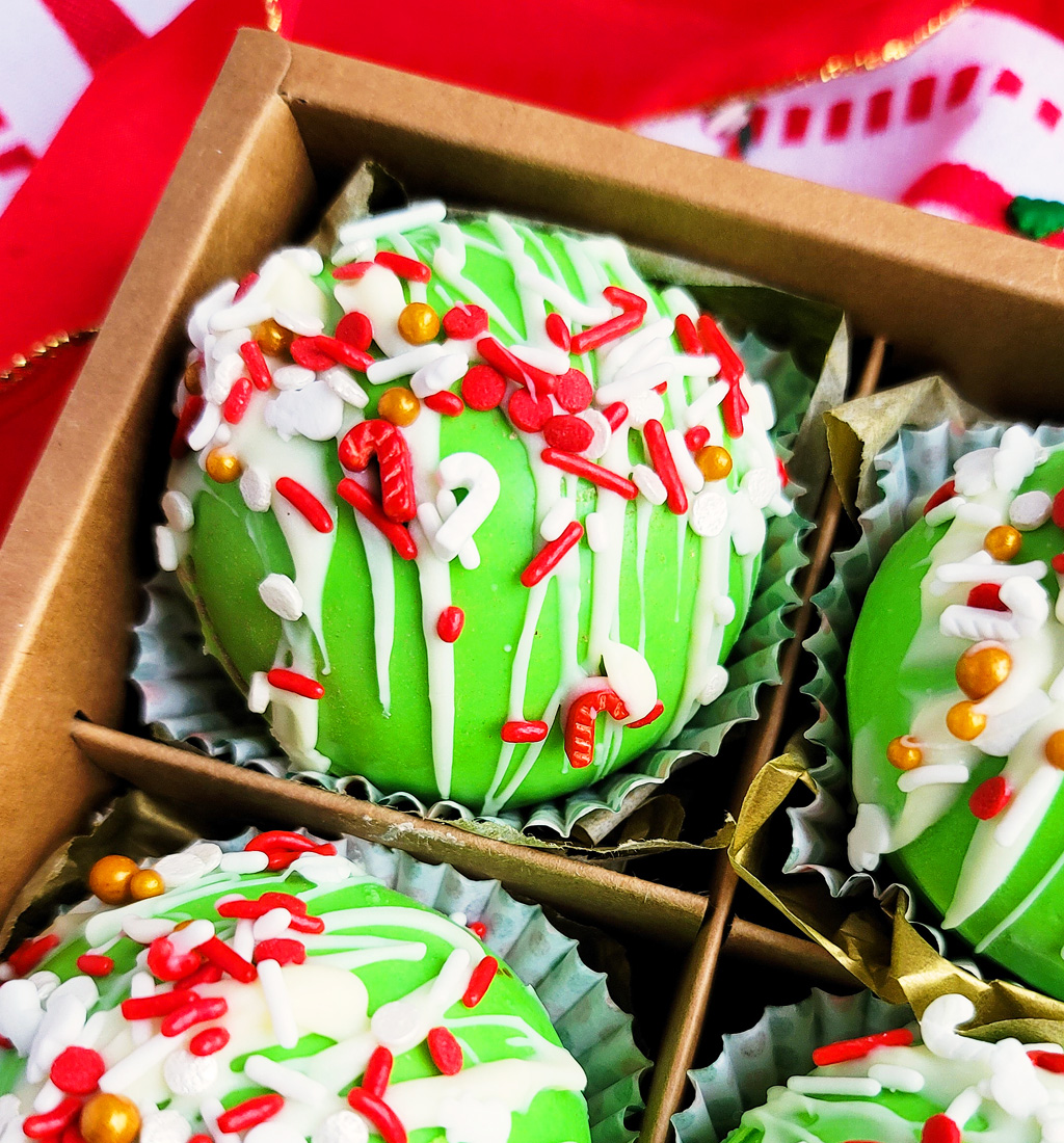 Green Grinch hot chocolate bombs with white chocolate drizzled on top, with Christmas sprinkles. DIY Hot chocolate bomb recipe. www.littleeatsandthings.com