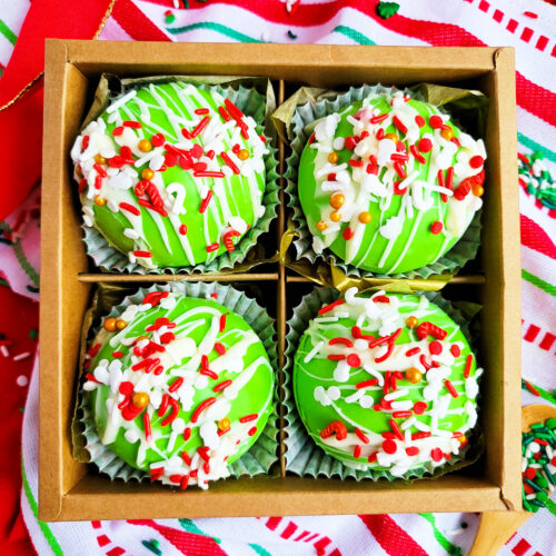 Green Grinch hot chocolate bombs with white chocolate drizzled on top, with Christmas sprinkles. DIY Hot chocolate bomb recipe. www.littleeatsandthings.com