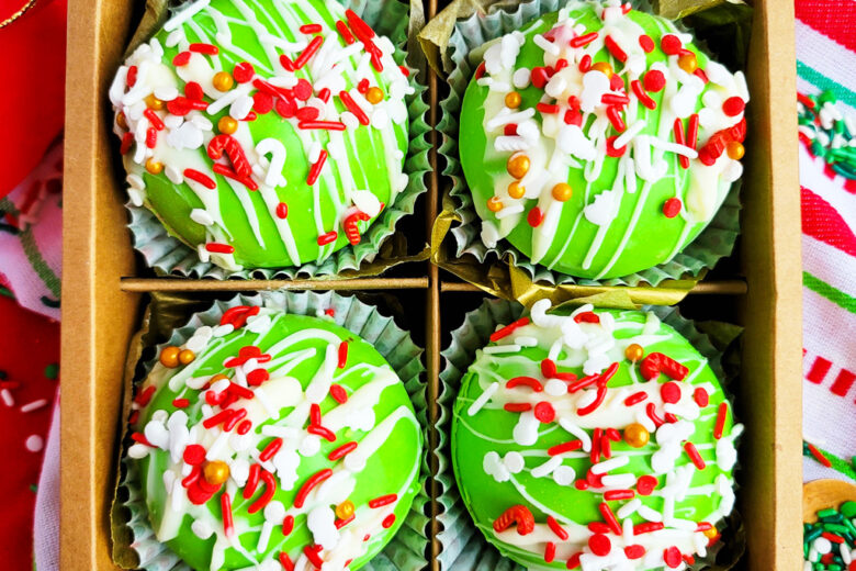 Green Grinch hot chocolate bombs with white chocolate drizzled on top, with Christmas sprinkles. DIY Hot chocolate bomb recipe. www.littleeatsandthings.com