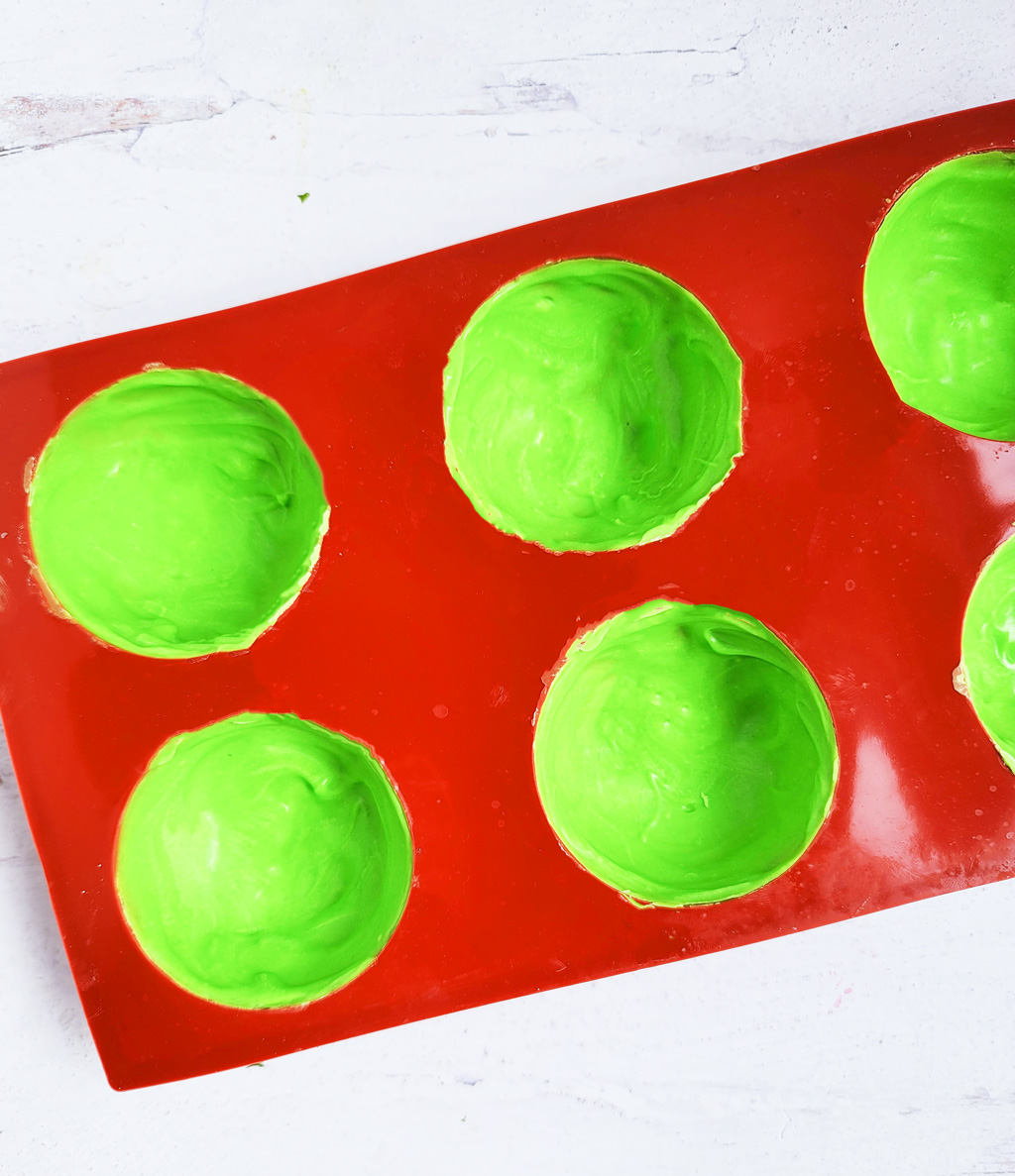 Green Grinch hot chocolate bombs with white chocolate drizzled on top, with Christmas sprinkles. DIY Hot chocolate bomb recipe. www.littleeatsandthings.com