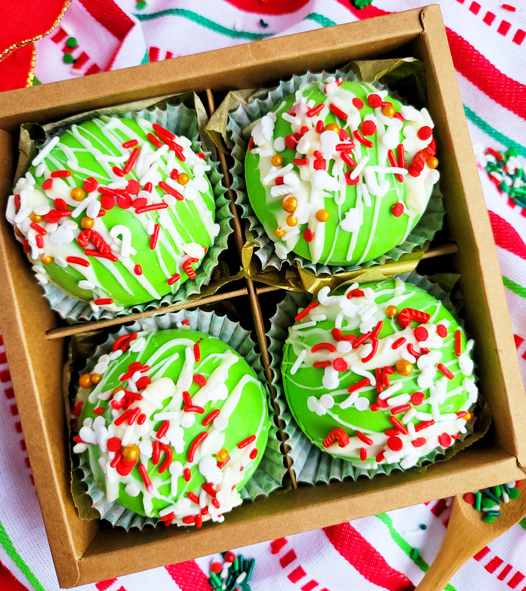 Green Grinch hot chocolate bombs with white chocolate drizzled on top, with Christmas sprinkles. DIY Hot chocolate bomb recipe. www.littleeatsandthings.com