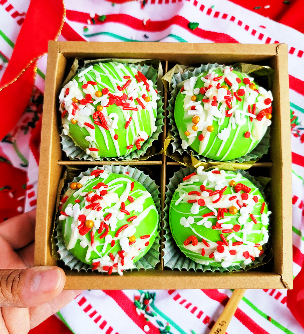 Green Grinch hot chocolate bombs with white chocolate drizzled on top, with Christmas sprinkles. DIY Hot chocolate bomb recipe. www.littleeatsandthings.com