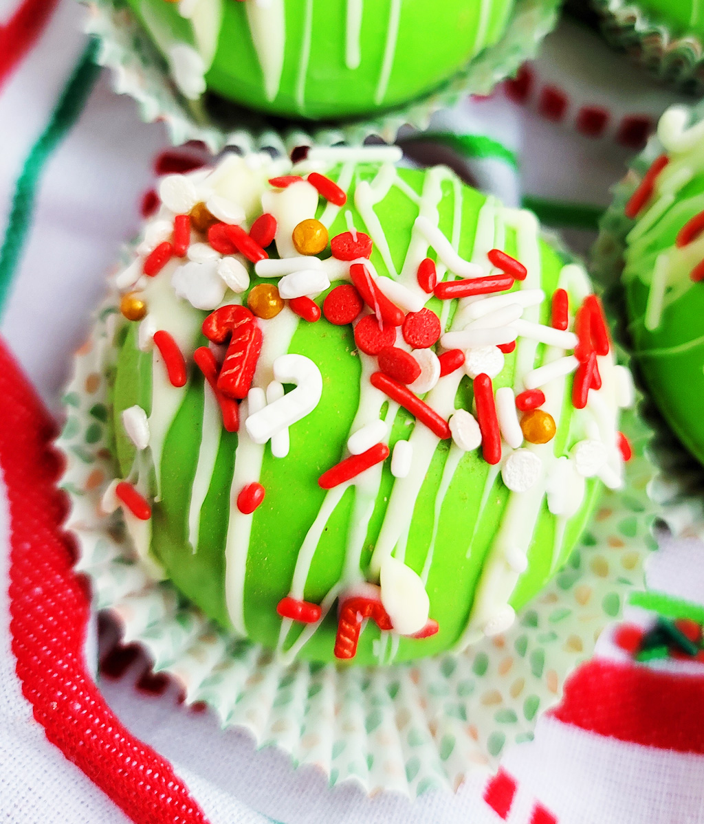 Green Grinch hot chocolate bombs with white chocolate drizzled on top, with Christmas sprinkles. DIY Hot chocolate bomb recipe. www.littleeatsandthings.com