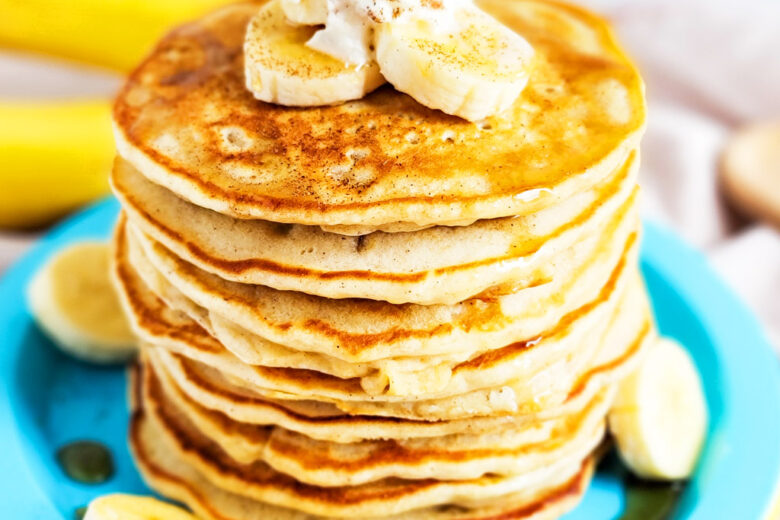 banana pancakes with syrup topped with sliced bananas, whipped cream, and cinnamon littleeatsandthings.com