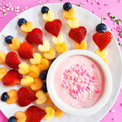 heart-shaped fruit skewers on a white plate on a pink surface for Valentine's Day littleeatsandthings.com