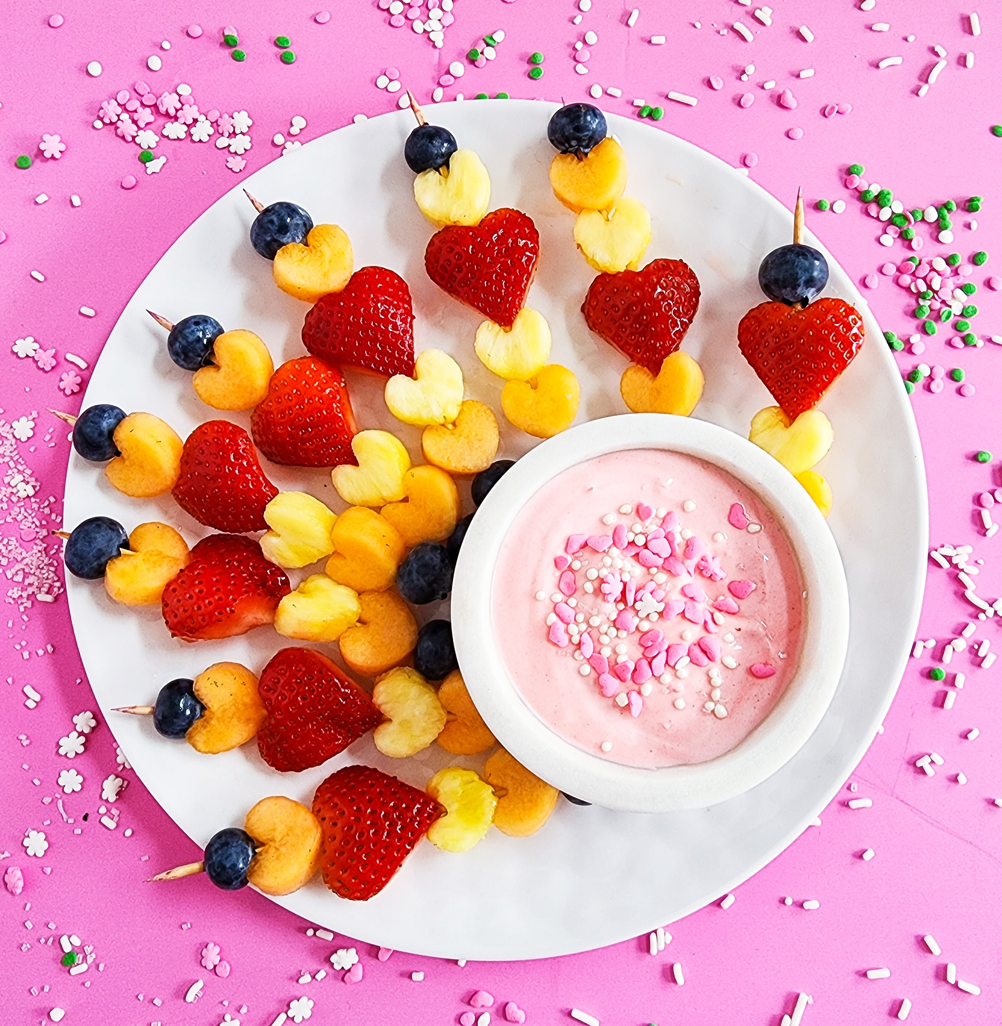 heart-shaped fruit skewers on a white plate on a pink surface for Valentine's Day littleeatsandthings.com