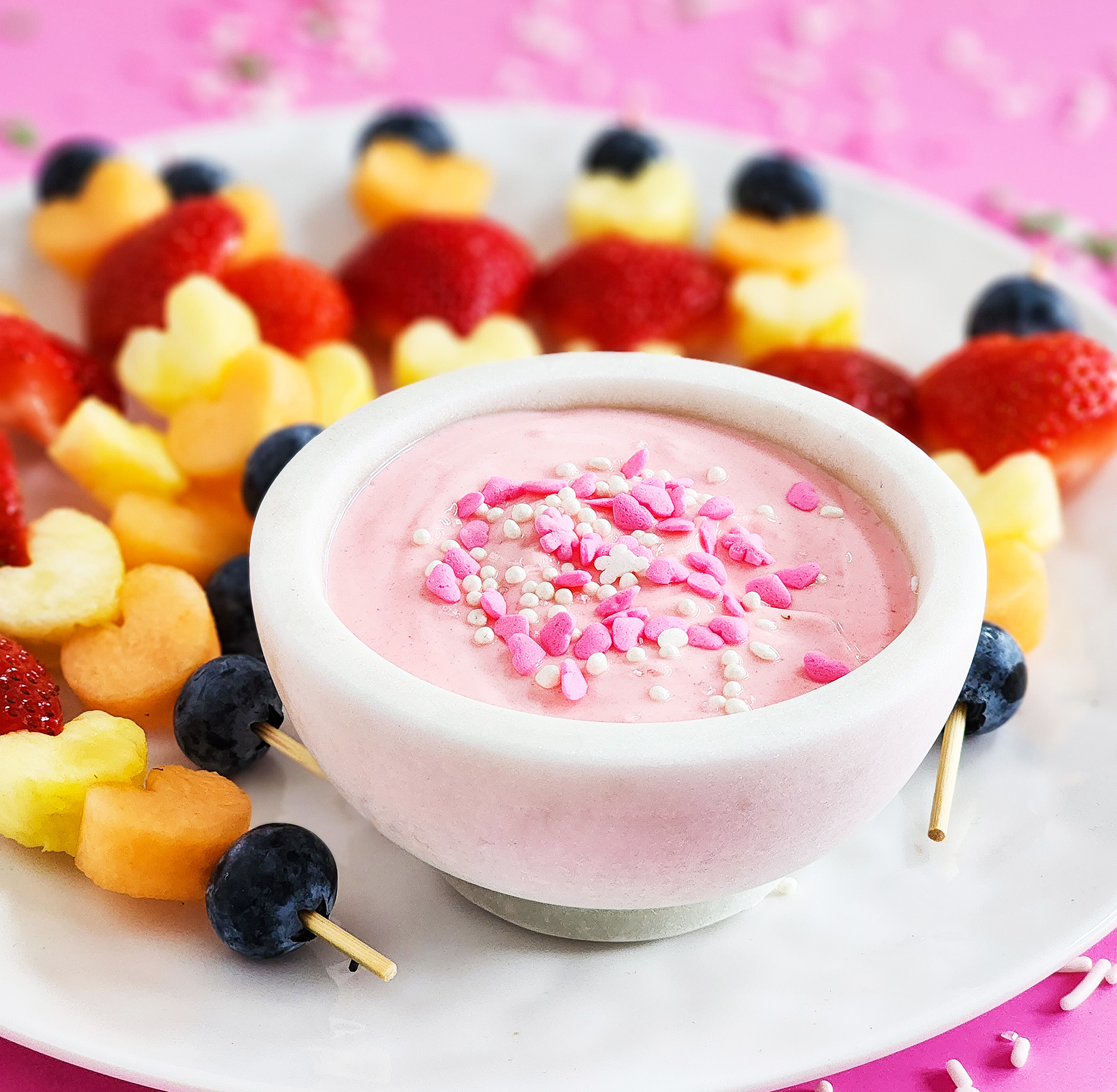 heart-shaped fruit skewers on a white plate on a pink surface for Valentine's Day littleeatsandthings.com