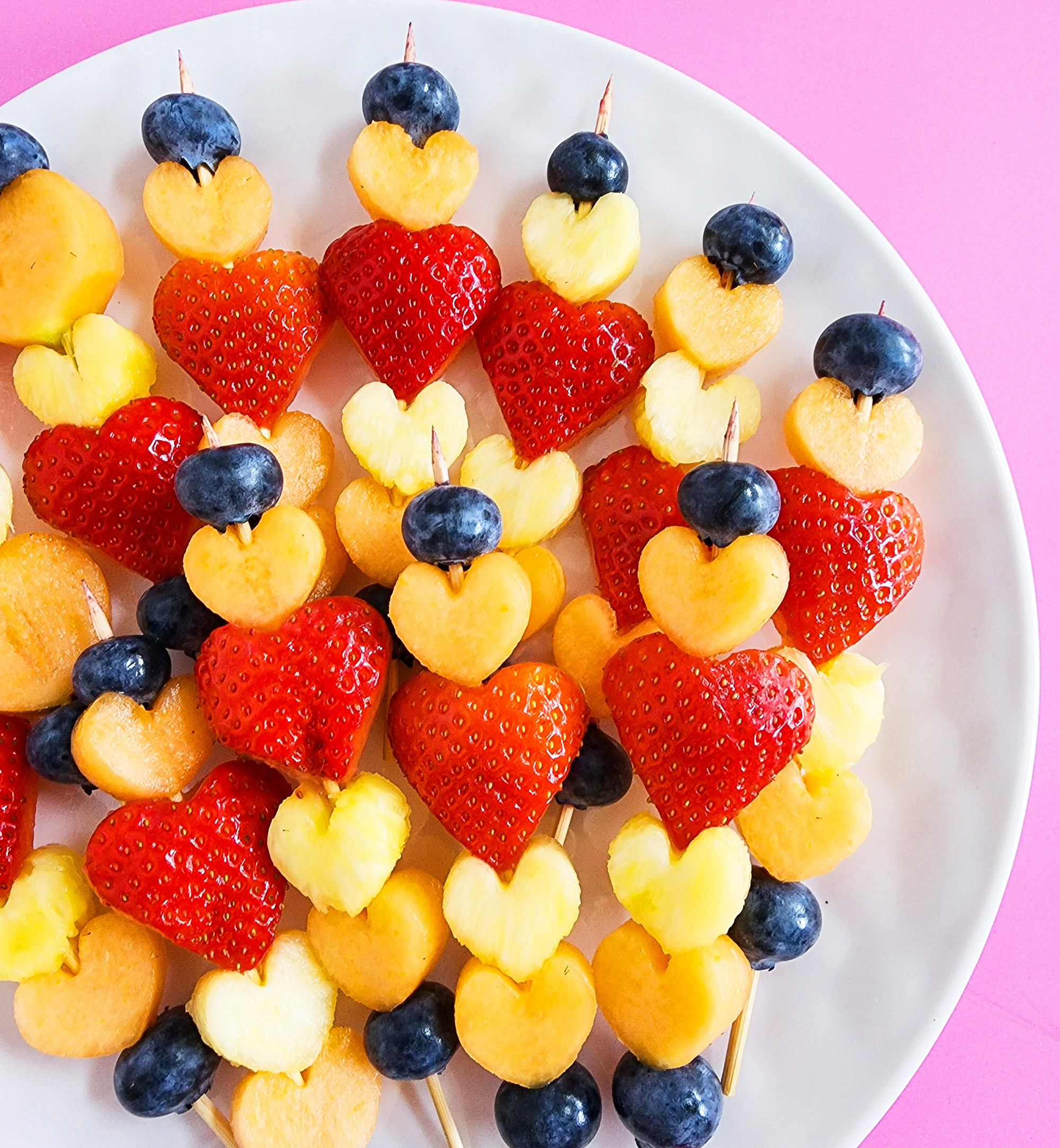 heart-shaped fruit skewers on a white plate on a pink surface for Valentine's Day littleeatsandthings.com