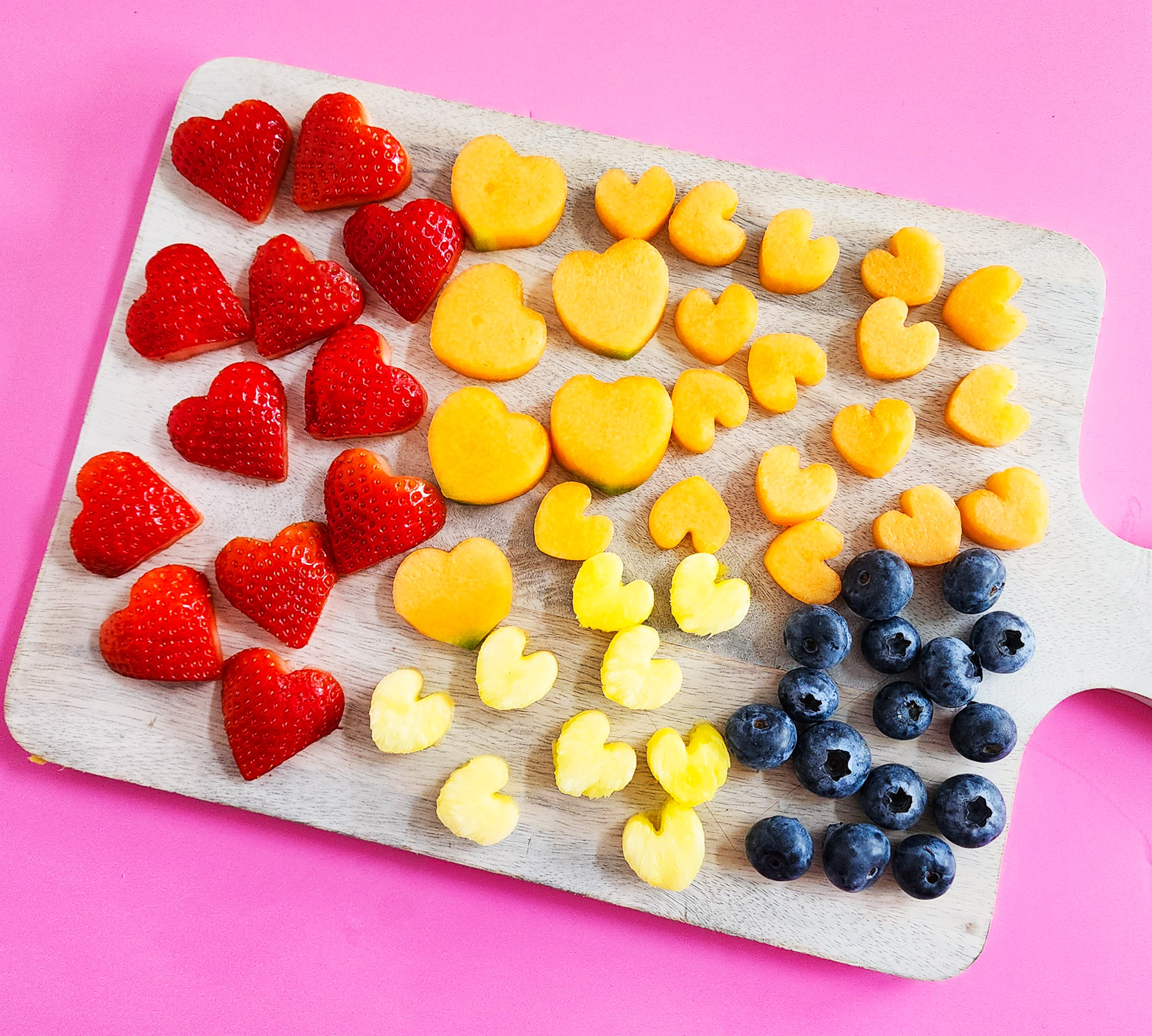 heart-shaped fruit skewers on a white plate on a pink surface for Valentine's Day littleeatsandthings.com